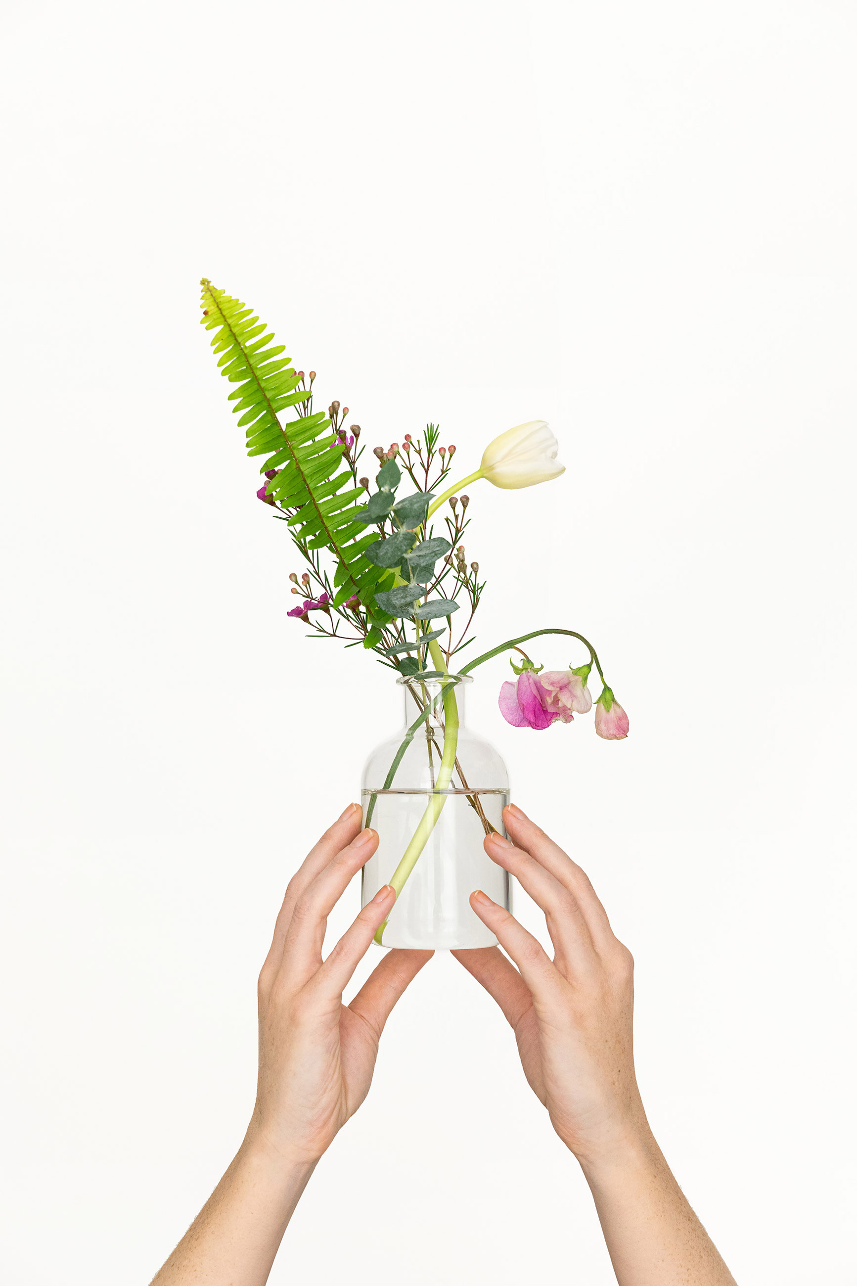Hands holding a glass vase with modern flower arrangement